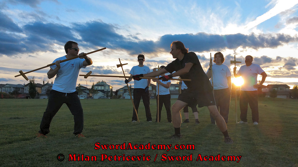 Milan demonstrates during an outdoor class in front of Sword Academy students and the setting sun poleaxe exercise / drill using dague to thrust in a composite attack inspired by historical sources from the French (and German) medieval (and renaissance) tradition, part of Sword Academy HEMA / WMA / Martial Arts curriculum.