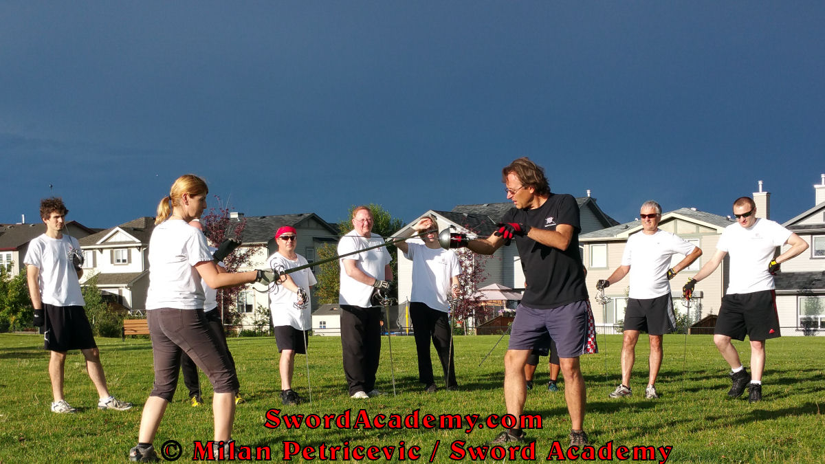 Milan demonstrates during an outdoor class with the stormy skies in background in front of Sword Academy students rapier exercise / drill using thrust from Quarta guard inspired by historical sources from the Italian renaissance tradition, part of Sword Academy HEMA / WMA / Martial Arts curriculum.