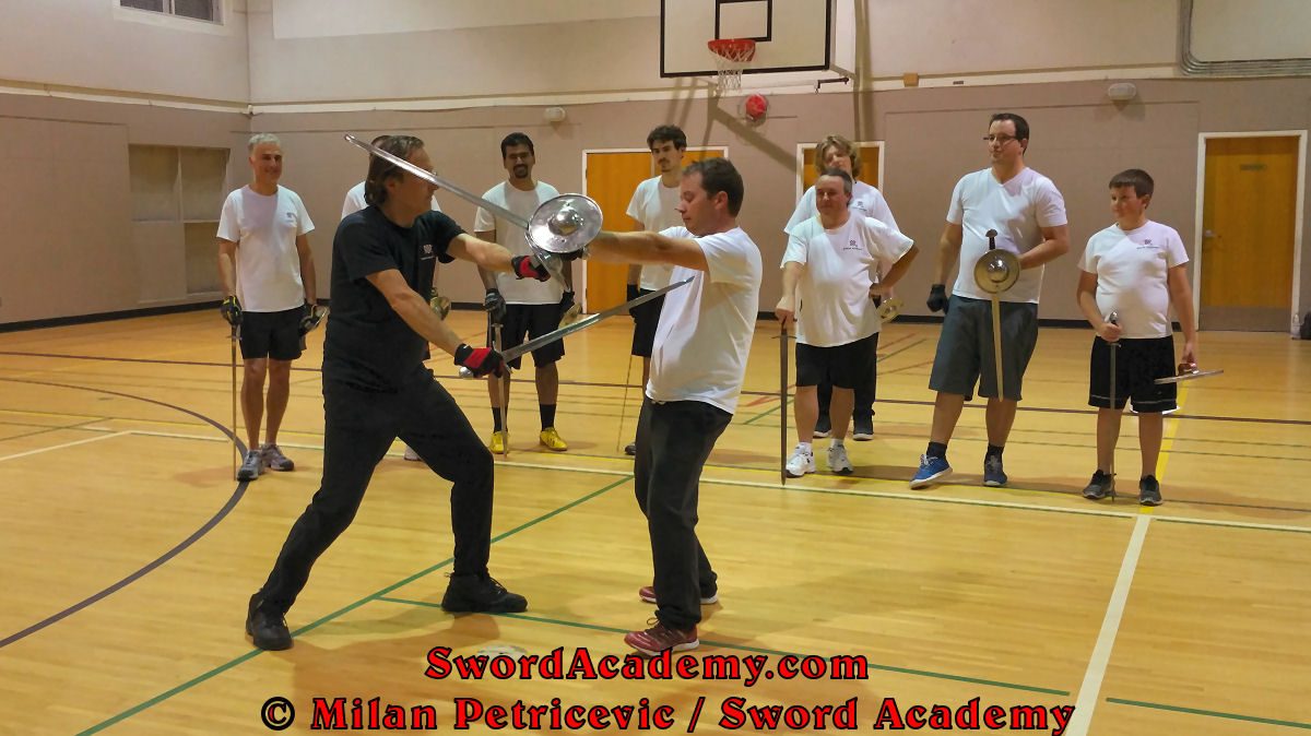 Milan demonstrates during an indoor class in front of Sword Academy students sword and buckler exercise / drill using followup rising thrust from the bind inspired by historical sources from the German medieval and renaissance tradition, part of Sword Academy HEMA / WMA / Martial Arts curriculum.