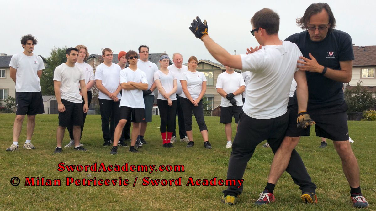 Milan demonstrates during an outdoor class in front of Sword Academy students wrestling exercise / drill using a throw from the third horizontal stance inspired by historical sources from the German medieval tradition, part of Sword Academy HEMA / WMA / Martial Arts curriculum.